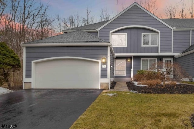 view of front of home featuring a garage, driveway, a yard, roof with shingles, and board and batten siding