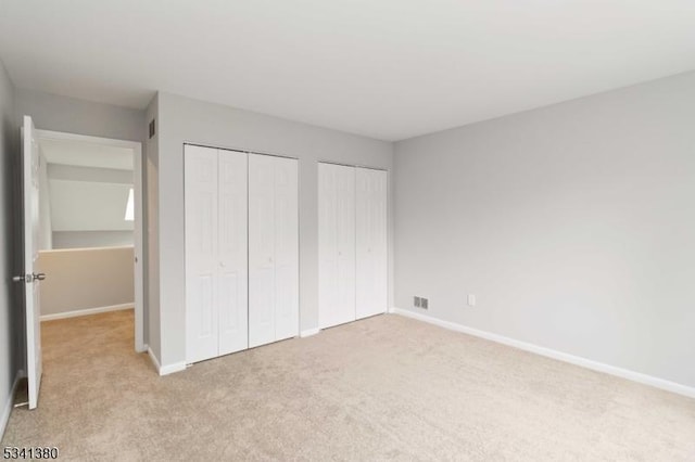 unfurnished bedroom with baseboards, visible vents, light colored carpet, and multiple closets