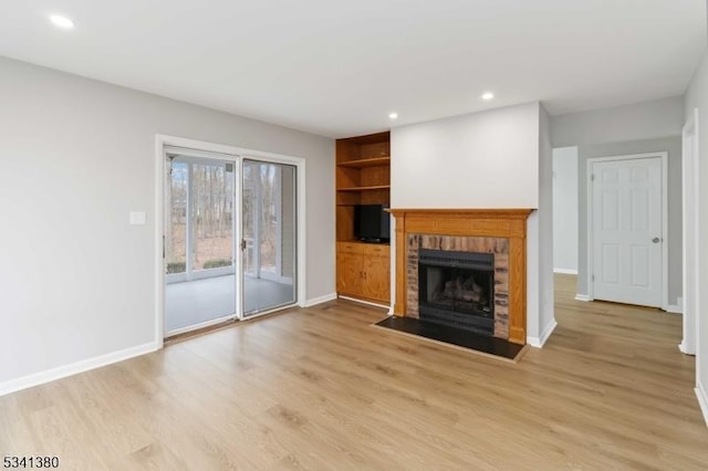 unfurnished living room with baseboards, light wood-type flooring, a brick fireplace, built in shelves, and recessed lighting