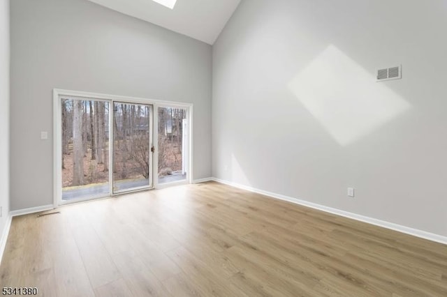 spare room with a skylight, baseboards, visible vents, wood finished floors, and high vaulted ceiling