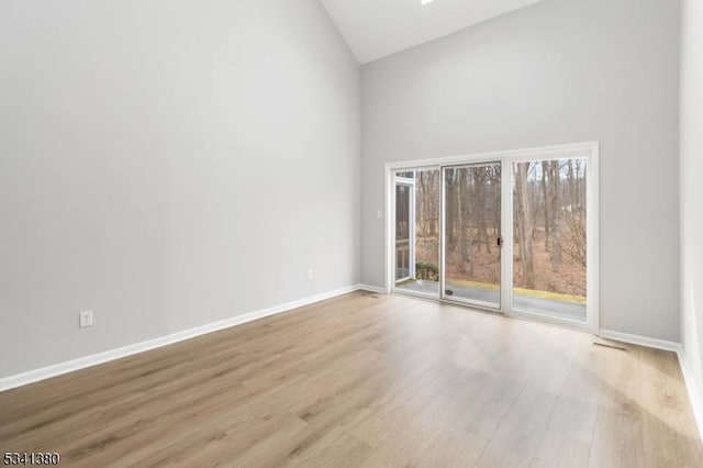 unfurnished room featuring a skylight, baseboards, high vaulted ceiling, and wood finished floors