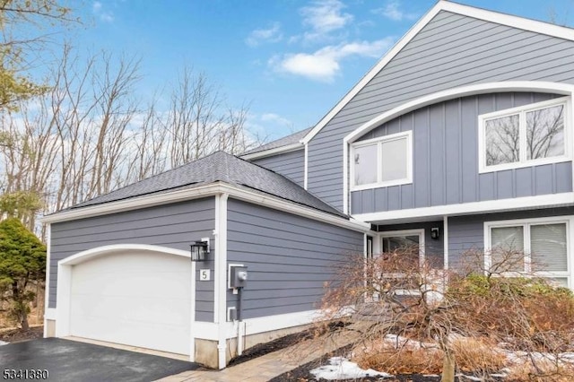 view of side of property with a garage, roof with shingles, and aphalt driveway