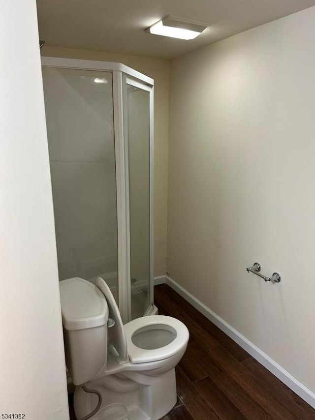 bathroom with a shower stall, wood finished floors, toilet, and baseboards