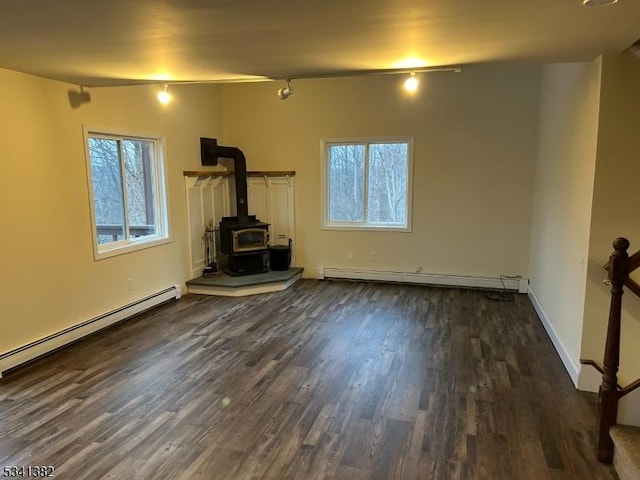 unfurnished living room with dark wood-style floors, a wealth of natural light, a wood stove, and baseboard heating