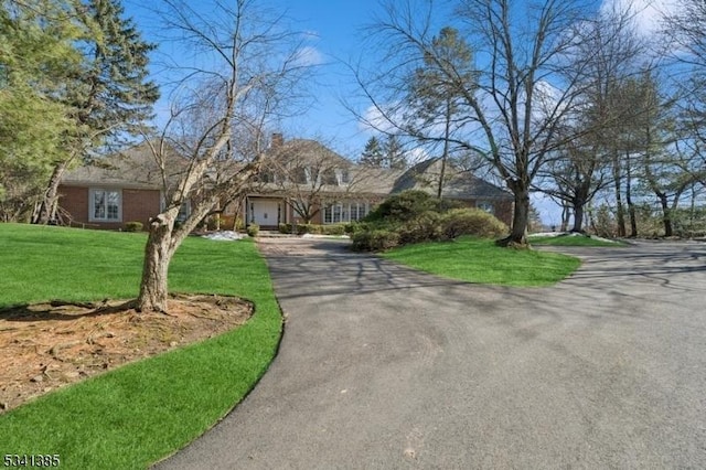 view of front facade with driveway, a chimney, and a front yard