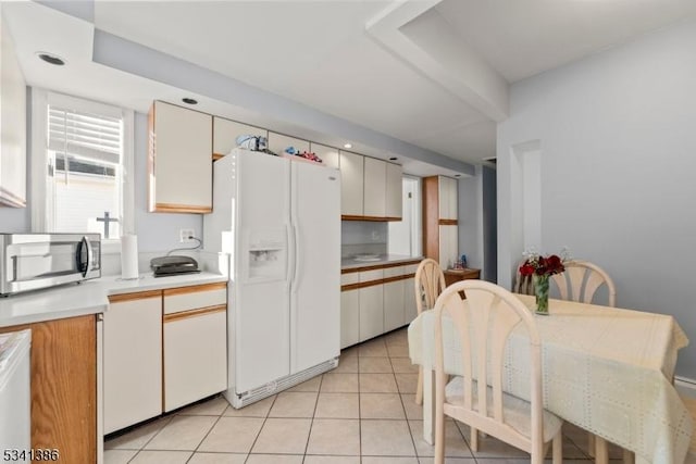 kitchen featuring light countertops, white refrigerator with ice dispenser, stainless steel microwave, and light tile patterned flooring