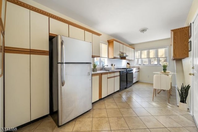 kitchen featuring range with gas stovetop, light countertops, freestanding refrigerator, a sink, and under cabinet range hood