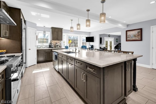 kitchen featuring stainless steel appliances, tasteful backsplash, a sink, wall chimney range hood, and dark brown cabinets