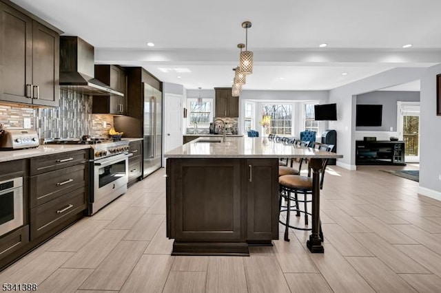 kitchen featuring a kitchen breakfast bar, wall chimney range hood, high quality appliances, and dark brown cabinetry