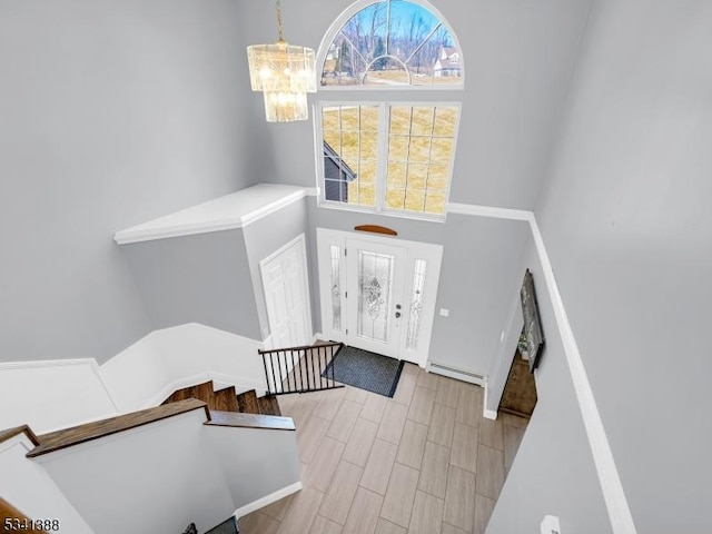 entryway featuring a notable chandelier, a baseboard heating unit, a high ceiling, wood finish floors, and stairs