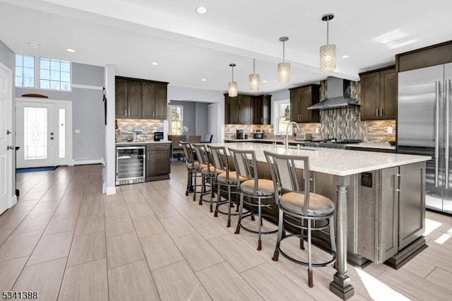 kitchen with beverage cooler, dark brown cabinetry, built in refrigerator, and wall chimney exhaust hood