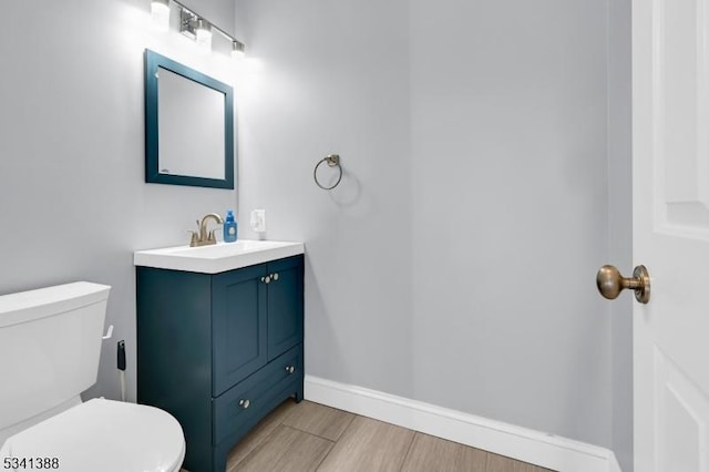 half bathroom with toilet, wood finished floors, vanity, and baseboards