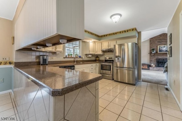 kitchen featuring under cabinet range hood, a peninsula, a sink, vaulted ceiling, and appliances with stainless steel finishes