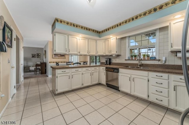 kitchen featuring light tile patterned floors, dark countertops, backsplash, stainless steel dishwasher, and a sink