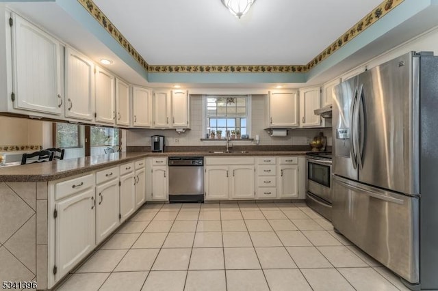 kitchen with light tile patterned flooring, a sink, appliances with stainless steel finishes, backsplash, and dark countertops