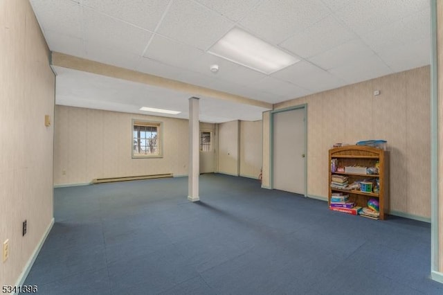 below grade area with wallpapered walls, baseboards, a baseboard heating unit, and a drop ceiling