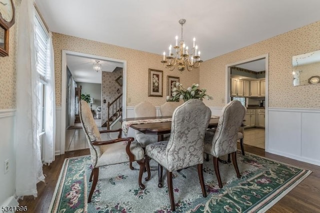 dining room featuring wallpapered walls, wainscoting, wood finished floors, stairs, and a notable chandelier