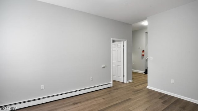 unfurnished room featuring a baseboard radiator, baseboards, and wood finished floors