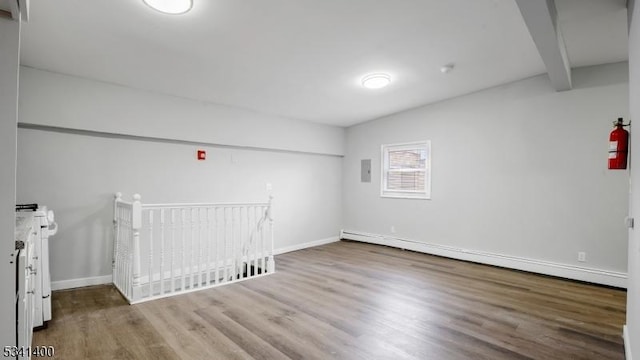 unfurnished room featuring beamed ceiling, baseboard heating, wood finished floors, and baseboards