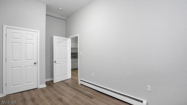 unfurnished bedroom featuring baseboards, baseboard heating, and wood finished floors