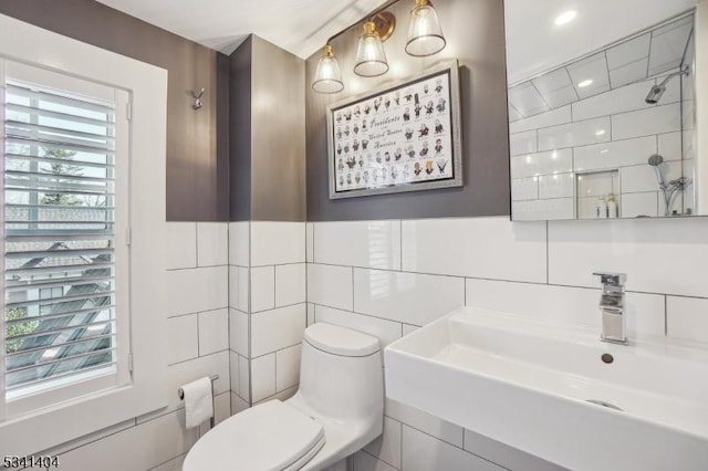 bathroom with tile walls, toilet, a tile shower, and a sink