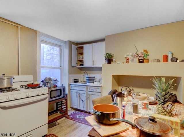 kitchen featuring open shelves, white gas stove, light countertops, light wood-style floors, and stainless steel microwave