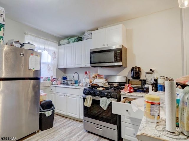 kitchen with light wood-style flooring, a sink, light countertops, appliances with stainless steel finishes, and white cabinetry