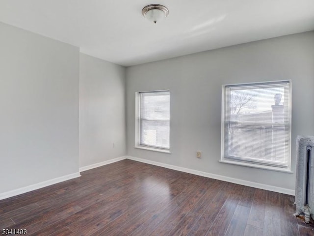 empty room featuring radiator heating unit, wood finished floors, and baseboards