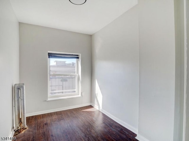 empty room featuring baseboards, wood finished floors, and radiator heating unit