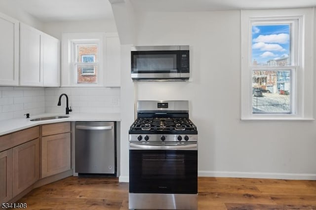 kitchen with wood finished floors, a sink, light countertops, appliances with stainless steel finishes, and decorative backsplash