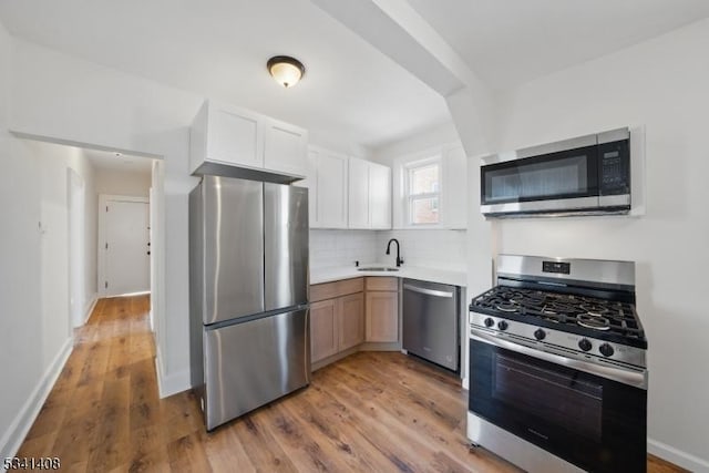 kitchen with stainless steel appliances, a sink, light countertops, light wood-type flooring, and tasteful backsplash