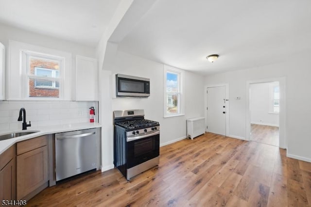 kitchen with a sink, light countertops, appliances with stainless steel finishes, backsplash, and light wood finished floors