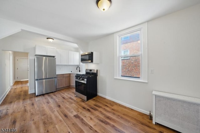 kitchen with baseboards, radiator heating unit, appliances with stainless steel finishes, light wood-type flooring, and backsplash