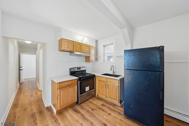 kitchen with stainless steel range with gas cooktop, a baseboard heating unit, freestanding refrigerator, a sink, and under cabinet range hood