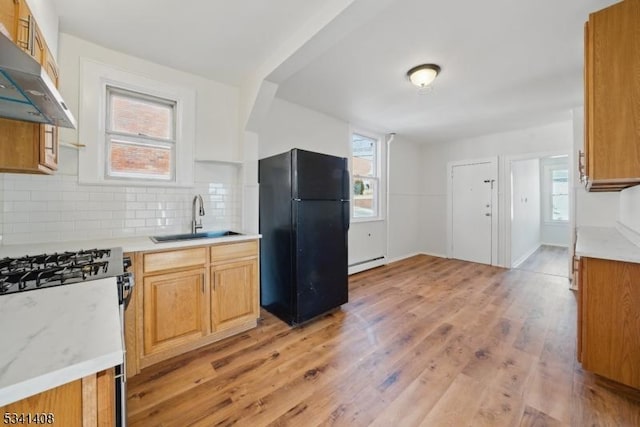 kitchen with light countertops, baseboard heating, freestanding refrigerator, a sink, and under cabinet range hood