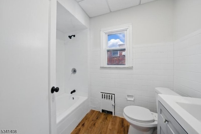 full bath with radiator, toilet, wood finished floors, vanity, and tile walls