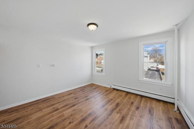 empty room with a baseboard heating unit, wood finished floors, and a healthy amount of sunlight