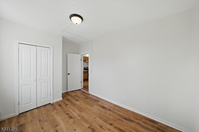 unfurnished bedroom with a closet, wood finished floors, and baseboards