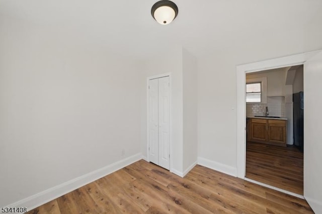 unfurnished bedroom with a sink, a closet, wood finished floors, and baseboards