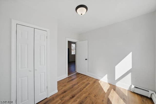 unfurnished bedroom featuring a closet, baseboards, baseboard heating, and wood finished floors