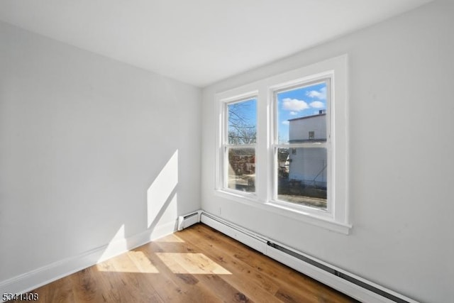 unfurnished room featuring baseboards, a baseboard heating unit, and wood finished floors