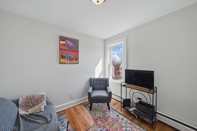 living area featuring a baseboard heating unit, baseboard heating, baseboards, and wood finished floors