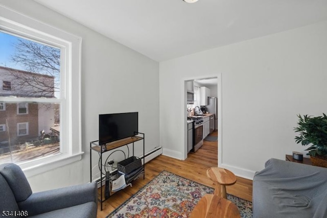 living area with light wood-style floors, a baseboard radiator, and baseboards