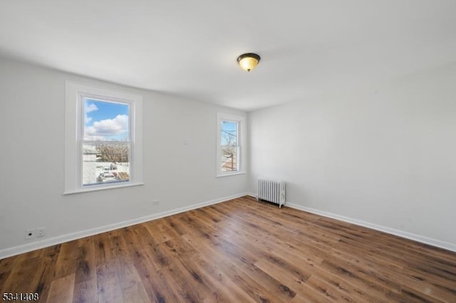 spare room featuring baseboards, wood finished floors, and radiator