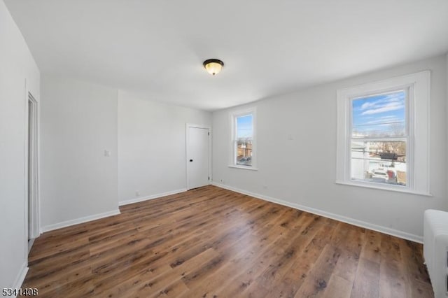 unfurnished bedroom featuring radiator, multiple windows, baseboards, and wood finished floors