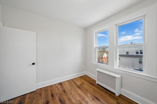 unfurnished room featuring radiator heating unit, baseboards, and wood finished floors