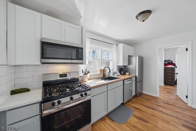 kitchen with stainless steel appliances, a sink, light countertops, light wood-type flooring, and tasteful backsplash