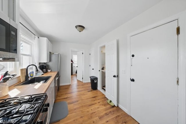 kitchen with appliances with stainless steel finishes, white cabinets, a sink, light wood-type flooring, and baseboards