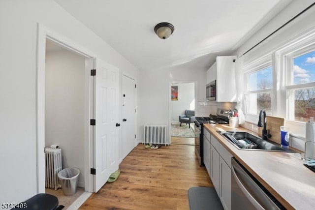 kitchen with stainless steel appliances, light countertops, a sink, and radiator heating unit