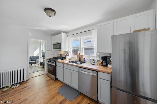 kitchen with radiator, appliances with stainless steel finishes, a sink, wooden counters, and backsplash